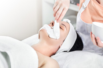 Wall Mural - The process of applying an alginate mask on the face of a woman. A female hands of a beautician holding spatula. Facial skin treatment in the beauty salon