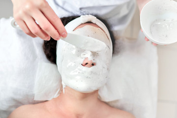 Wall Mural - Alginate mask application process. A female hands of a beautician holding spatula. Woman lying on a couch in the office of a cosmetologist. Facial skincare in the beauty salon