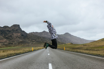 Wall Mural - young woman jumping on empty road in iceland with beautiful mountains on background