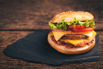 Close-up of delicious fresh home made burger with lettuce, cheese, onion and tomato on black stone and wood background