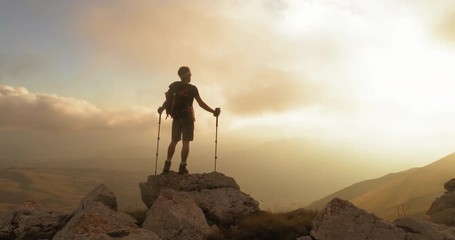 Wall Mural - young man hiker standing on ridge edge of the mountain in abruzzo italy with poles at sunset epic sh