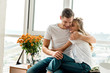 © LIGHTFIELD STUDIOS - happy young couple in love in casual clothing hugging at window at home