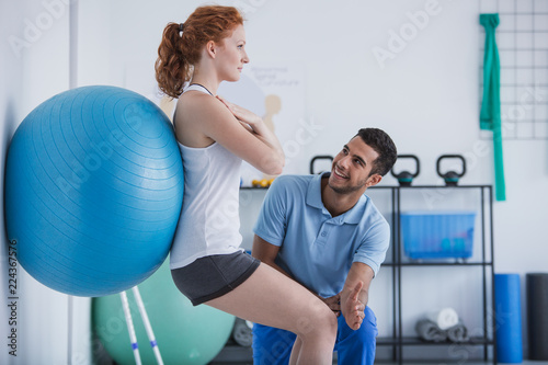 Fotografia Smiling professional personal trainer helping sportswoman exercising with ball