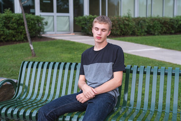 Wall Mural - Lonely teenager sitting on a bench outside of his high school.