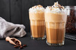 Iced caramel latte coffee in a tall glass with chocolate syrup and whipped cream. Dark wooden background.