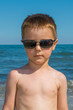 © nedomacki - a beautiful little boy posing on a beach by the sea with sunglasses