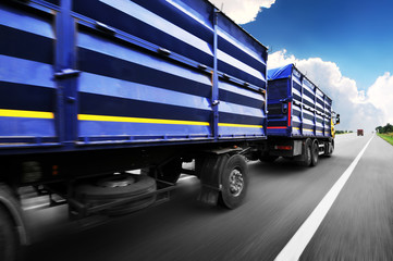 Truck in motion with a container driving on the countryside road against blue sky