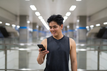 Young happy Asian man using phone at the subway station
