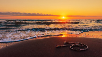 A piece of fishing rope on the beach at amazing colorful sunrise