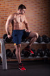 Muscular man stands near the counter with dumbbells in the gym.