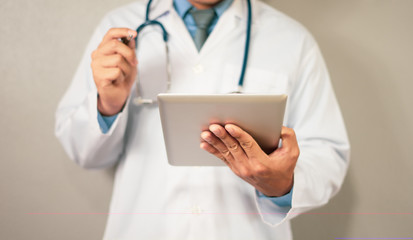 Doctor with digital tablet.  Asian young female doctor in white lab coat working on digital tablet and smiling while standing against grey background