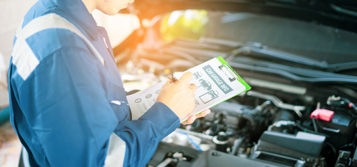 car service, repair, maintenance  concept - Asian auto mechanic man or Smith writing to the clipboard at workshop or warehouse, technician doing the checklist for repair machine a car in the garage