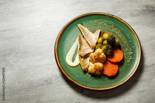 Fotografía top view on tasty hake fillet with vegetables and sauce served on green plate