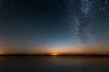 Blue Night Starry Sky With Milky Way Galaxy Above Lake And Russian Village. Night Glowing Stars