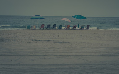 Beach chairs that sit low to the ground are lines up on the beach and ready for the vacationers to sit upon them and enjoy their beautiful day by the sea and sand