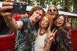 © Drobot Dean - Photo of joyous hipsters men and women smiling, and taking selfie on mobile phone near vintage minivan into the nature