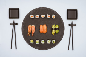 Wall Mural - top view of various delicious sushi on slate board and chopsticks isolated on white