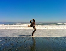 Driftwood Hand Coming Out Of Beach With Waves And Blue Sky