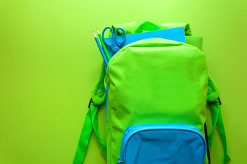 Wall Mural - Back to school concept. Green backpack with school supplies on green background. Top view. Copy space