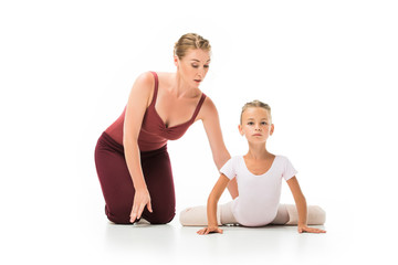 Wall Mural - focused female trainer helping little ballerina stretching isolated on white background