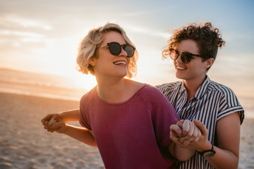 laughing lesbian couple dancing playfully on a beach at sunset