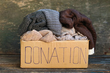 Donation Box With Warm Things On Old Wooden Background.