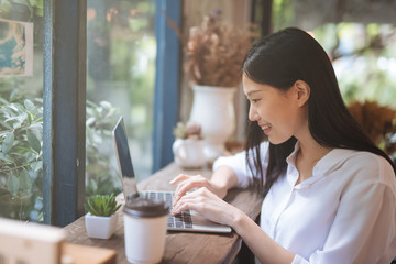 Wall Mural - Happy young Asian girl working at a coffee shop with a laptop