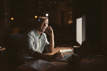 Wall Mural - Smiling Asian businessman talking on his cellphone late at night