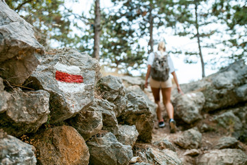 Wall Mural - hiking trail sign on rock and tourist woman walking on path