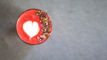 Fashionable strawberry latte, latte art and flower petals on foam, grey background.