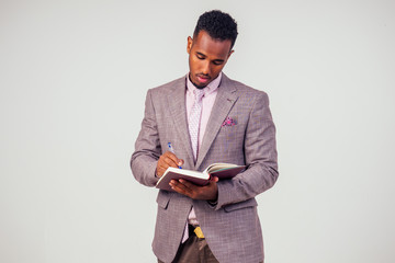 full length young afro american business man gray suit standing and holding notebook on white backgr