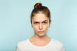 emotion face. frowning grumpy woman with pursed lips and piercing glance. young beautiful brown haired girl portrait on blue background.