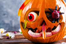 Orange Pumpkin Carved Into Jack O Lantern With Eyeball Candy And Gummy Worms & Spiders On Wooden Table. Background, Copy Space, Close Up, Top View. Halloween Party Decoration. Trick Or Treat Concept.