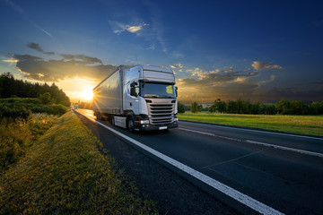 Wall Mural - white trucks arriving on the asphalt road in rural landscape in the rays of the sunset