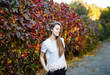 © Мария Балчугова - Bright autumn portrait. A young attractive brunette in a stylish raincoat walks in the Park in the autumn. She expressively looks at the camera on the background of colorful red foliage and vine.