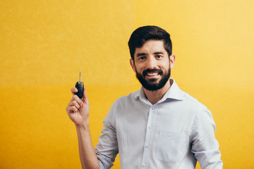 Wall Mural - Portrait of young man smiling and holding car keys. Isolated yellow background