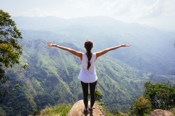 Sporty woman standing with raised arms on the top oh hill