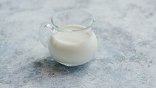 Closeup Shot Of Small Glass Cream Pitcher Full Of Fresh Milk On Marble Table
