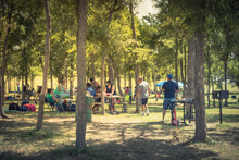 Blurred Large Group Of Friend, Family Members Enjoy Barbecue On Lakeside Area. Outdoor Camping At Natural Park With Picnic Table In Grand Prairie, Texas, USA. Outside Party And BBQ Concept