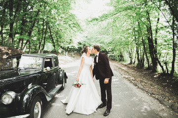 Beautiful newlywed couple posing near retro black car