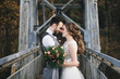 © ksyusha_yanovich - Happy young smiling bride and groom are standing on the suspension bridge. Wedding photos in an interesting place