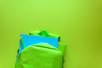 Wall Mural - Back to school concept. Green backpack with school supplies on green background. Top view. Copy space