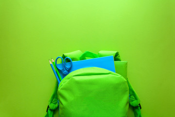 Wall Mural - Back to school concept. Green backpack with school supplies on green background. Top view. Copy space