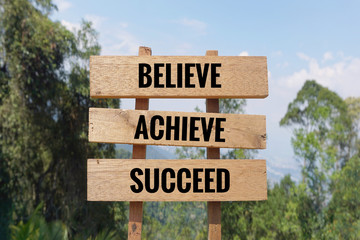 Motivational and inspirational quote - ‘BELIEVE, ACHIEVE, SUCCEED’ written on wooden signage. Blurred styled background.