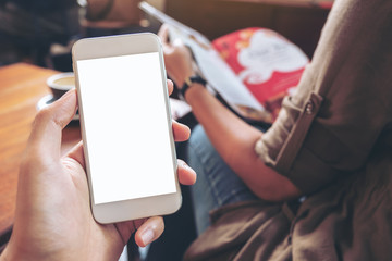 Mockup image of hand holding white mobile phone with blank screen with woman reading books in modern cafe