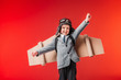 little emotional pilot in suit and cardboard plane wings with outstretched arms to fly isolated on red