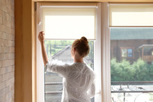Young Woman Opening Roller Curtains At Home