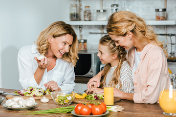 Wall Mural - child cutting vegetables for salad with mother and grandmother at home and chatting