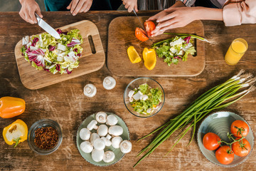 Wall Mural - cropped shot of women and child cutting vegetables for salad on rustic table