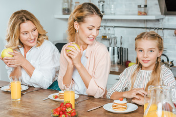 Wall Mural - happy little child with mother and grandmother having pancakes for breakfast at home